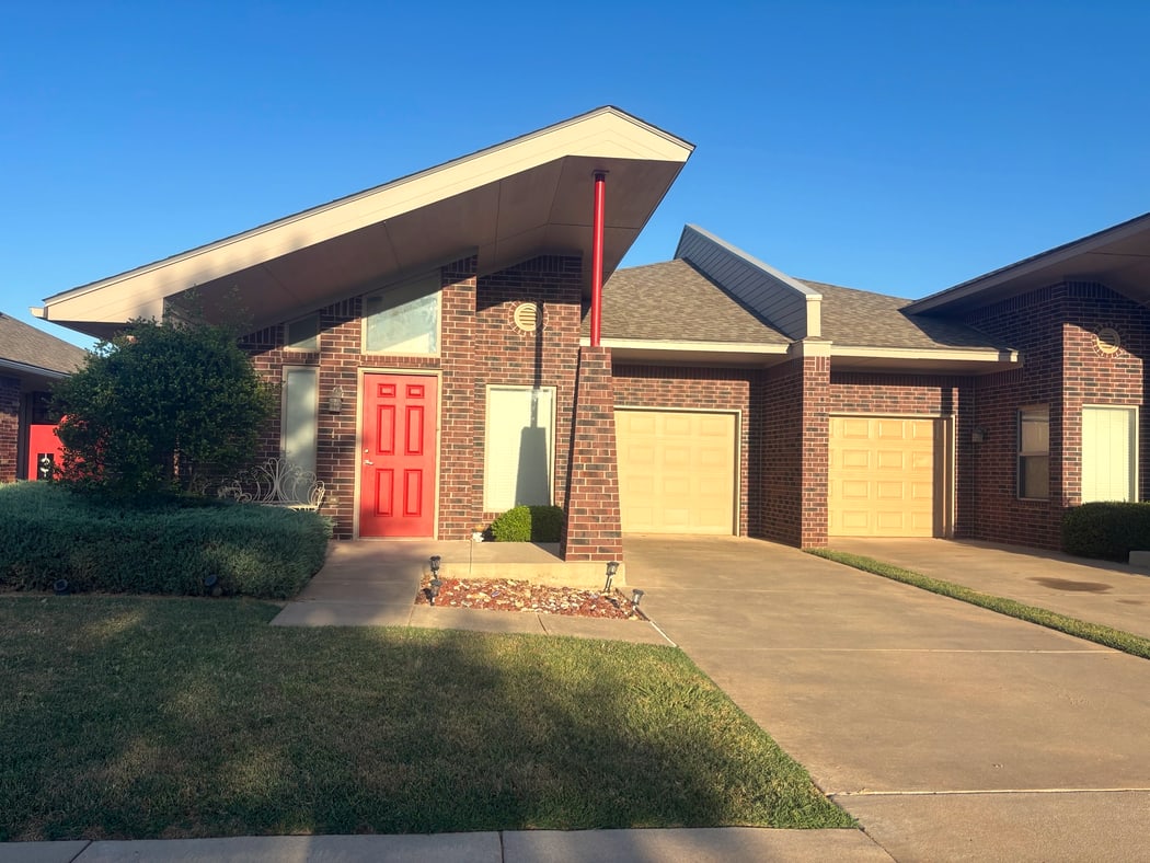 Front of a Forest Village duplex with red door, brick porch, and attached one-car garages