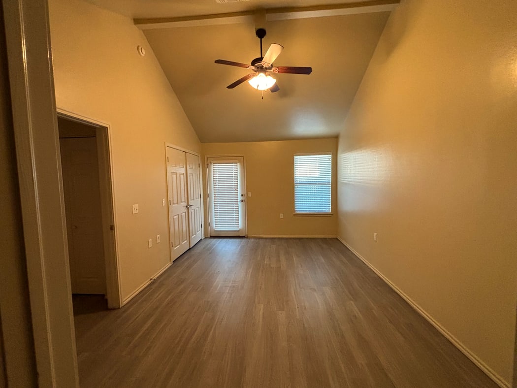 Living and dining room with vaulted ceiling, ceiling fan, double closet, and glass door to the patio